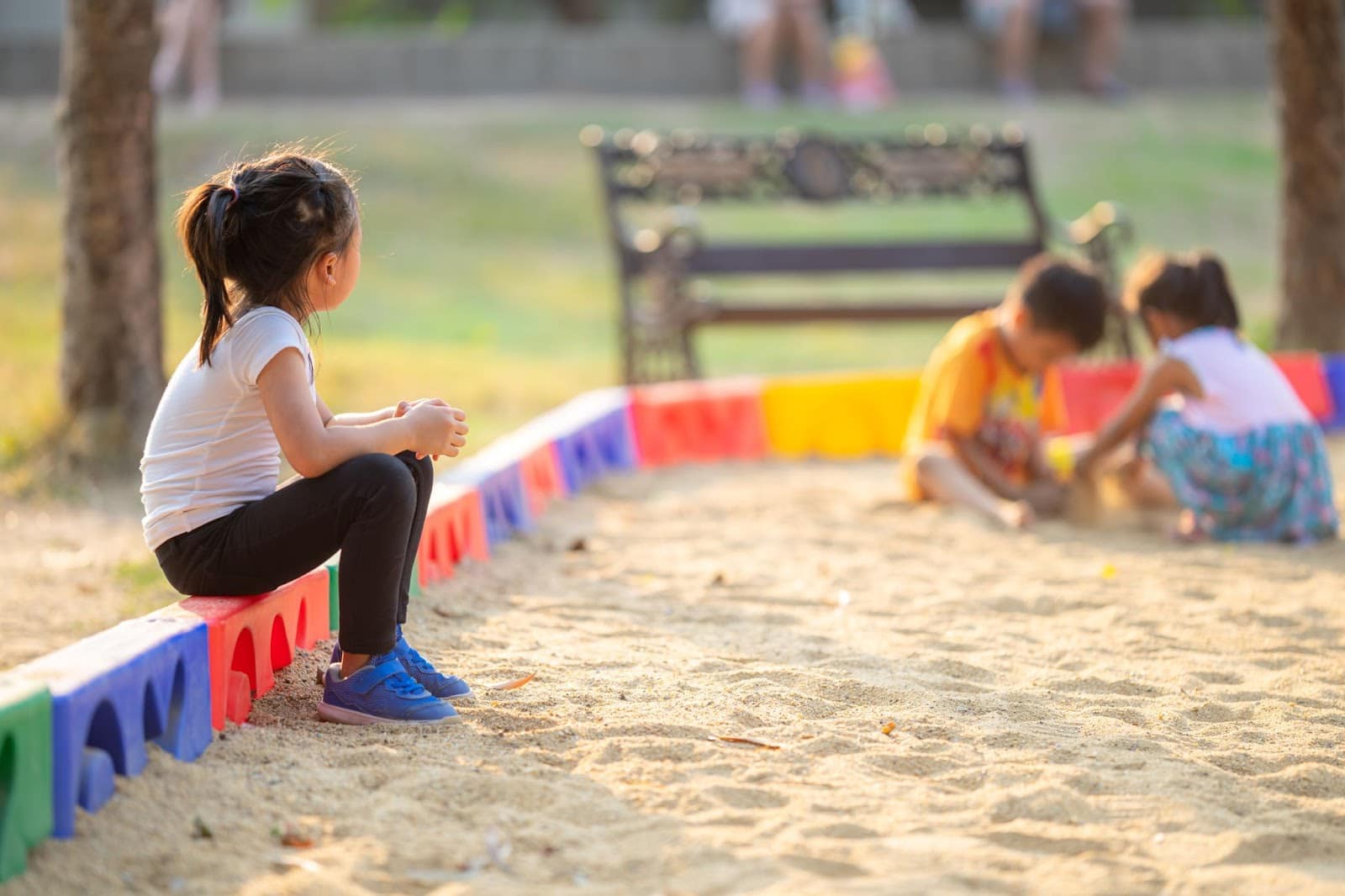 Young girl sitting alone in the park showing signs of speech delay and autism.